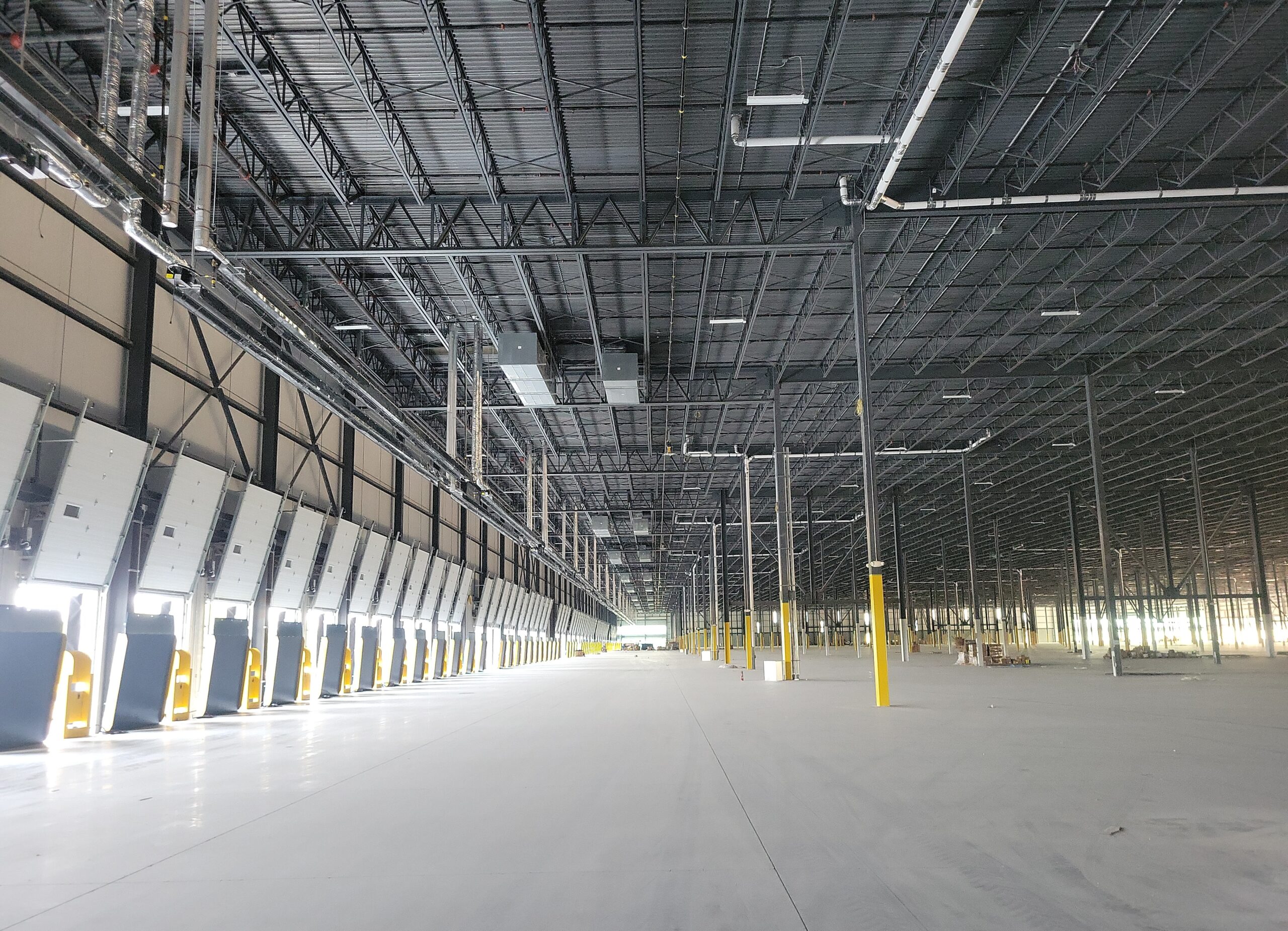 Interior view of a large warehouse showing rows of loading dock doors, a high open ceiling, and structural steel framing.