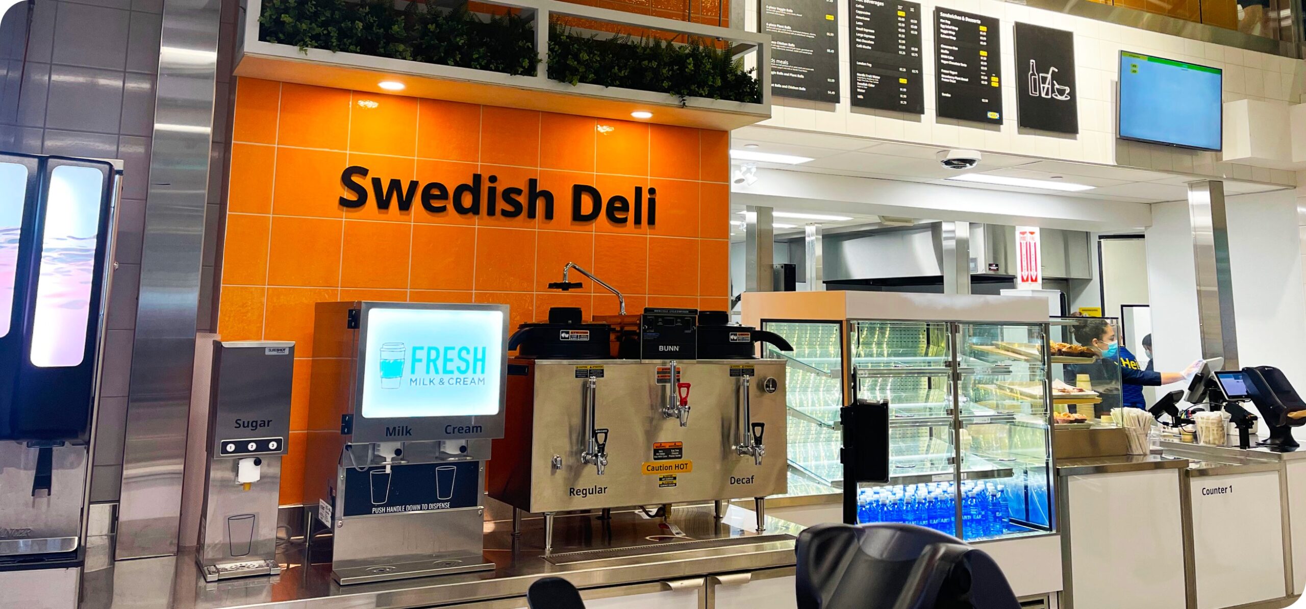 Interior view of the IKEA Swedish Deli counter with bright orange signage, food displays, and refrigerated items.