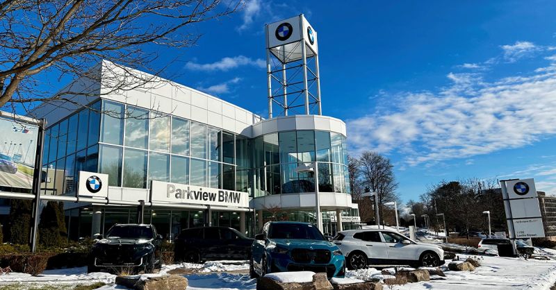 Contemporary BMW dealership with a glass showroom and tall BMW-branded tower, surrounded by parked vehicles on a snowy winter day.
