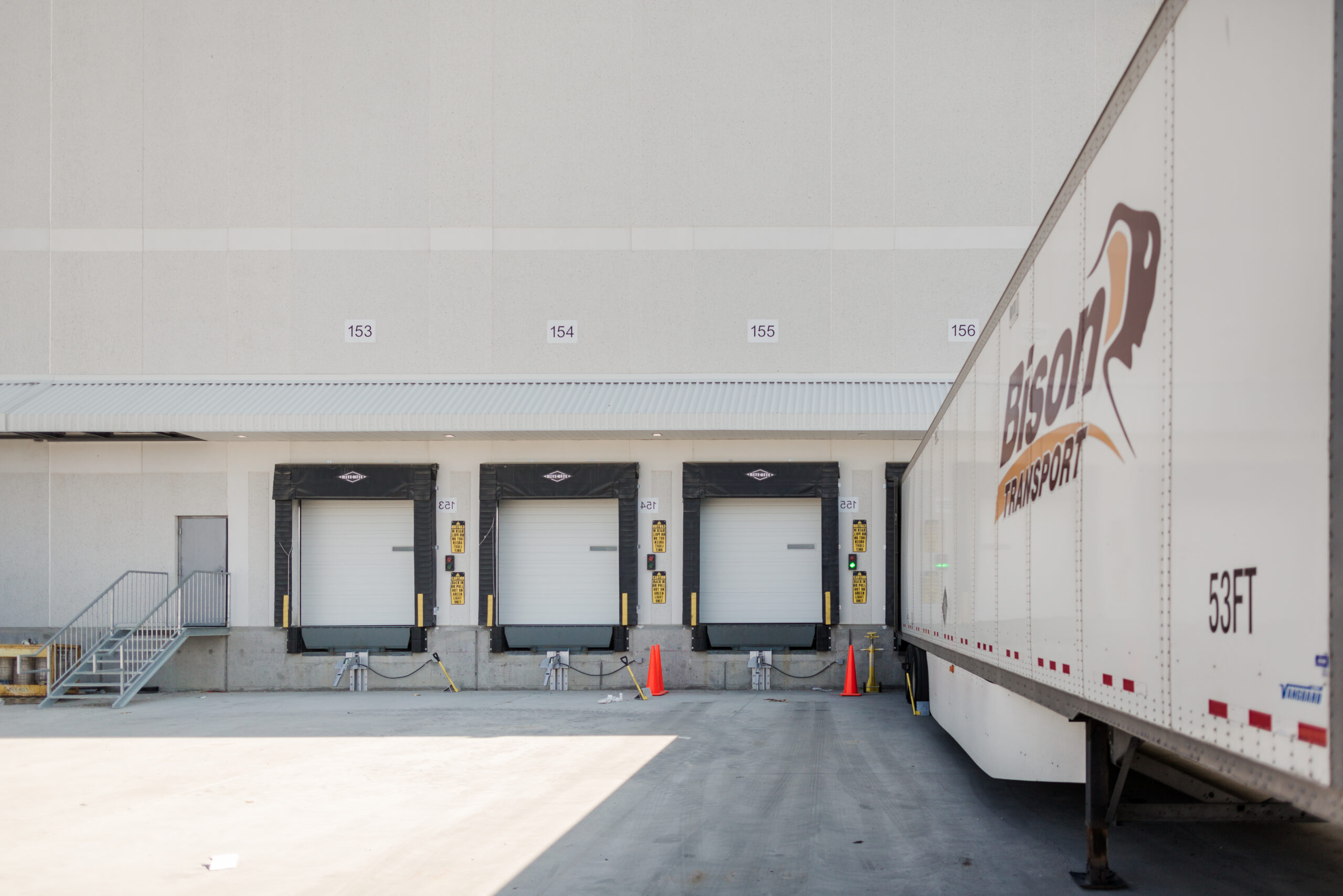 Three loading dock doors at a distribution facility with a transport trailer parked beside them.