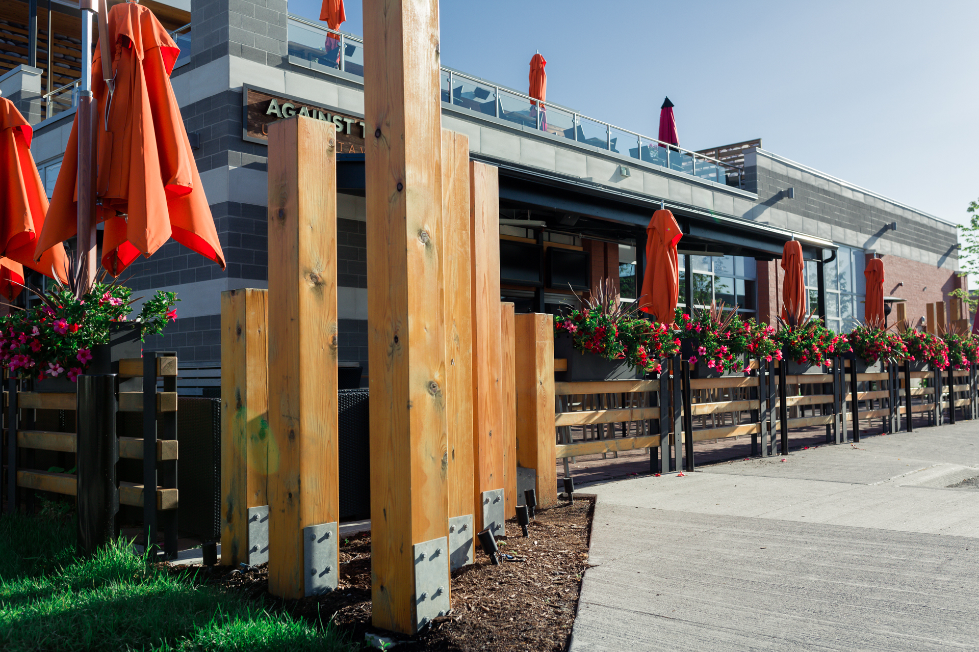 Outdoor restaurant patio with wooden fencing, orange umbrellas, and bright floral planters.