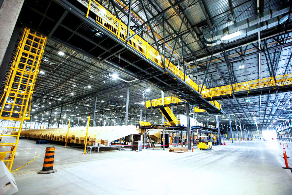 Interior view of a large warehouse with extensive yellow steel walkways, conveyors, and high ceilings, part of the Canadian Tire Bolton Distribution Centre.