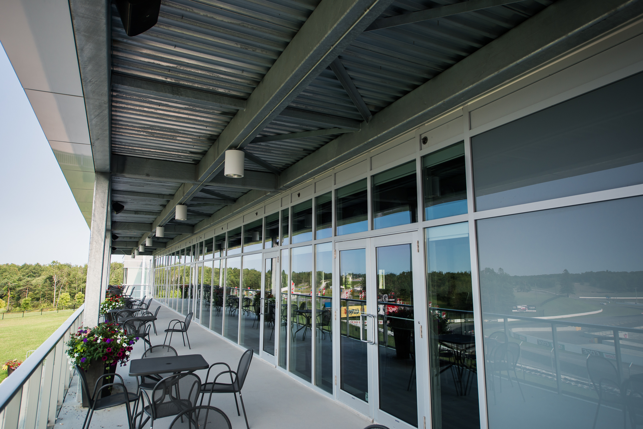 Covered outdoor terrace with metal tables and chairs, overlooking the surrounding landscape through glass-paneled walls.