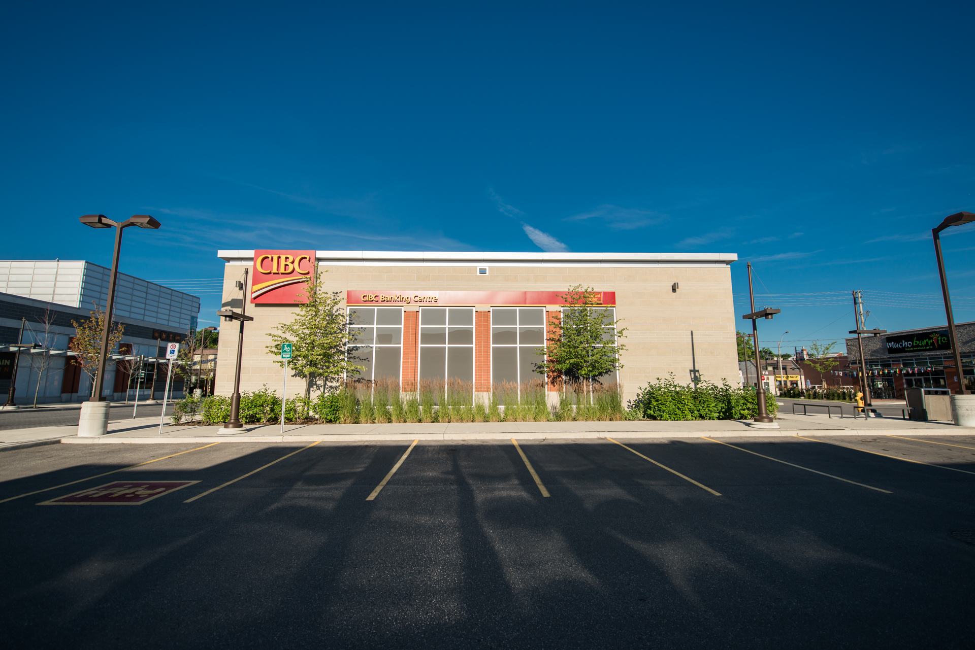 Front view of a standalone CIBC branch with large windows and landscaped greenery under a clear sky.