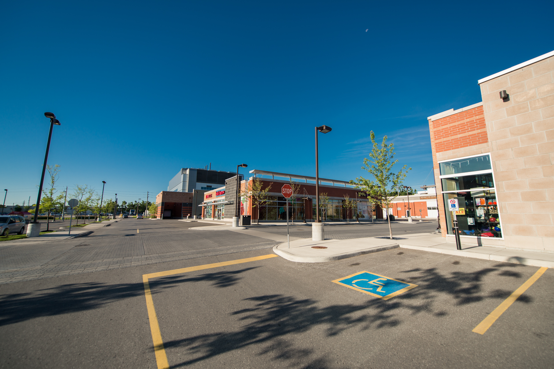 Wide view of a retail centre parking lot with storefronts, accessible parking, and clear blue skies.