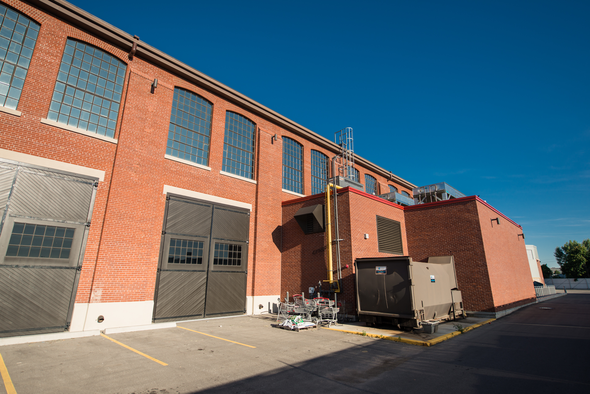 Rear view of a brick industrial-style building with tall windows and exterior mechanical equipment.
