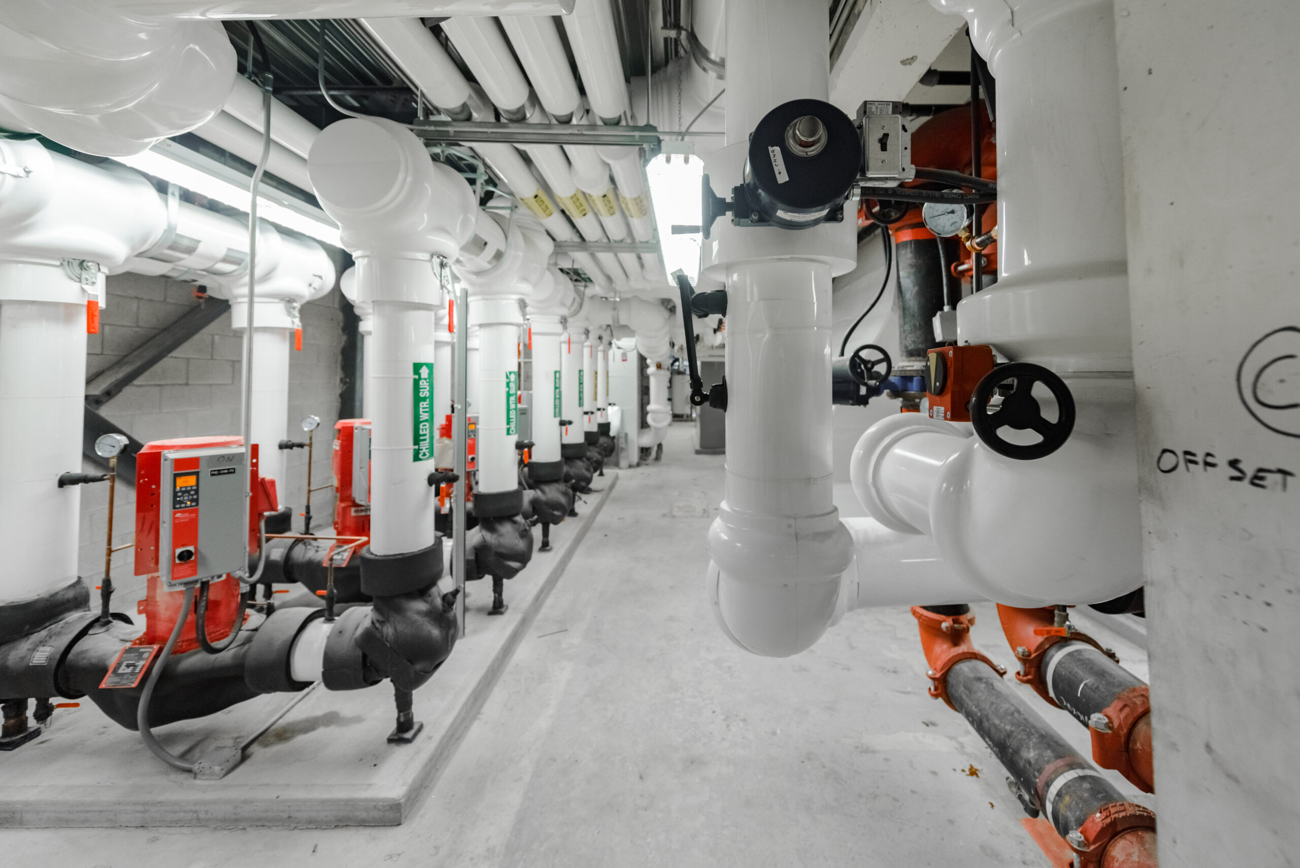 Mechanical room with insulated white piping, pumps, valves, and industrial mechanical equipment.