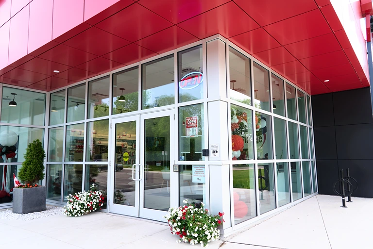 Glass entrance of an Apple Self Storage building with red exterior panels, potted plants, and clear signage.