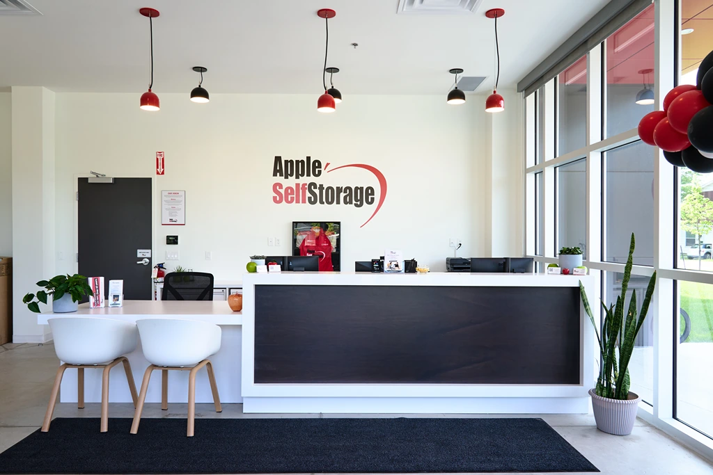 Interior of the Apple Self Storage office showing a front desk, seating area, pendant lighting, and large windows.