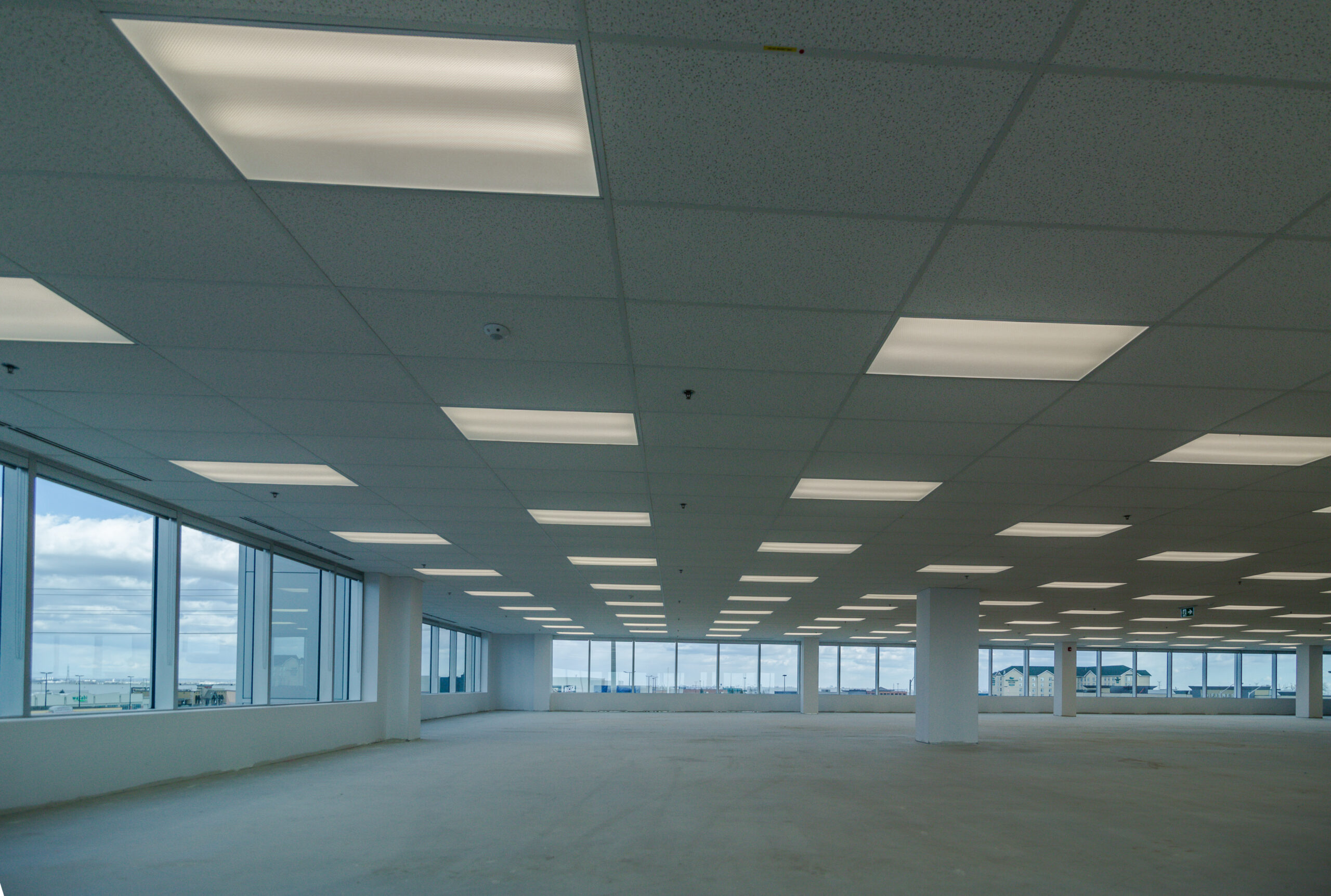 Empty interior office space with large windows, open floor layout, and ceiling lighting.
