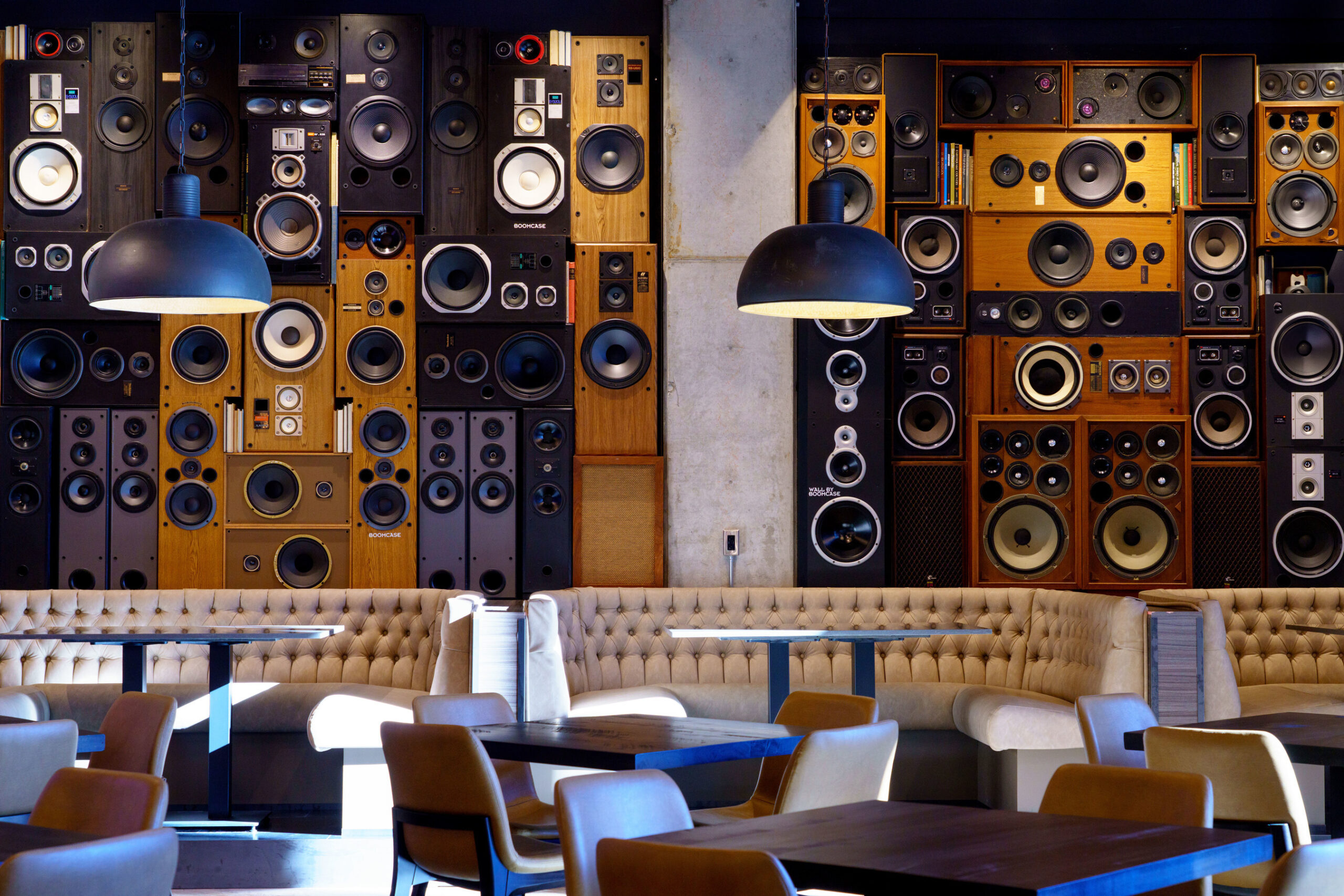Restaurant seating area with tables, booths, and a decorative wall of speakers.