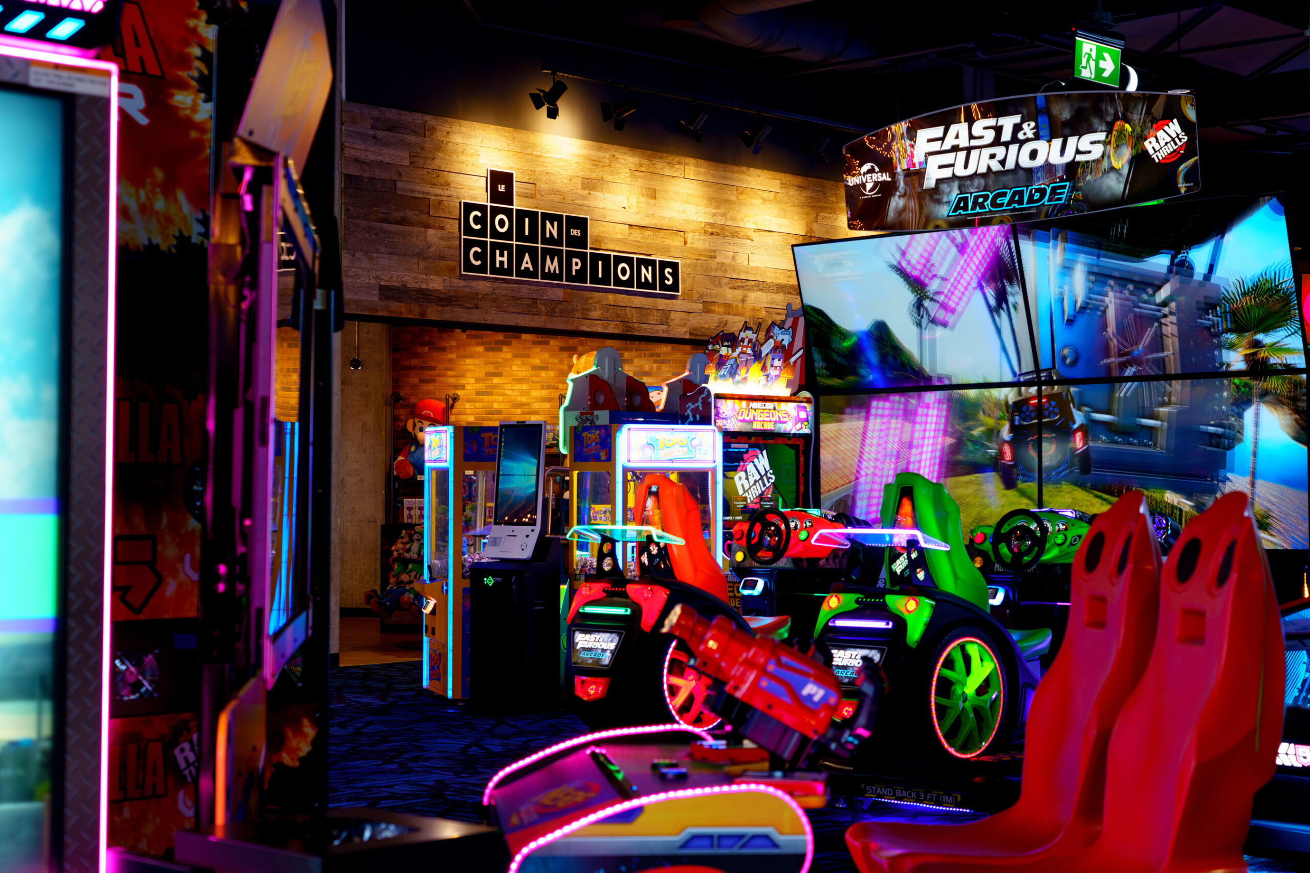 Arcade area with illuminated racing games and large digital screens.