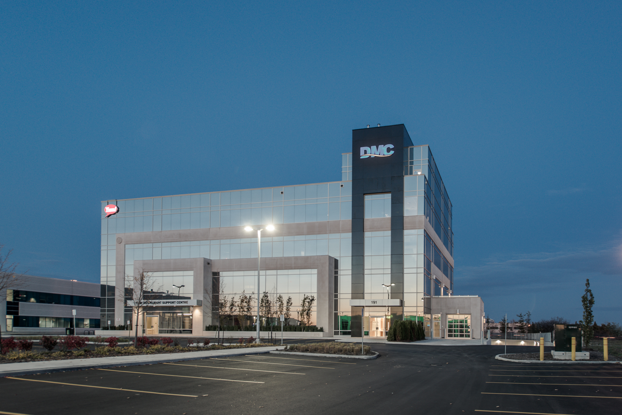 Exterior view of the DMC office building with glass façades, illuminated signage, and surrounding parking.
