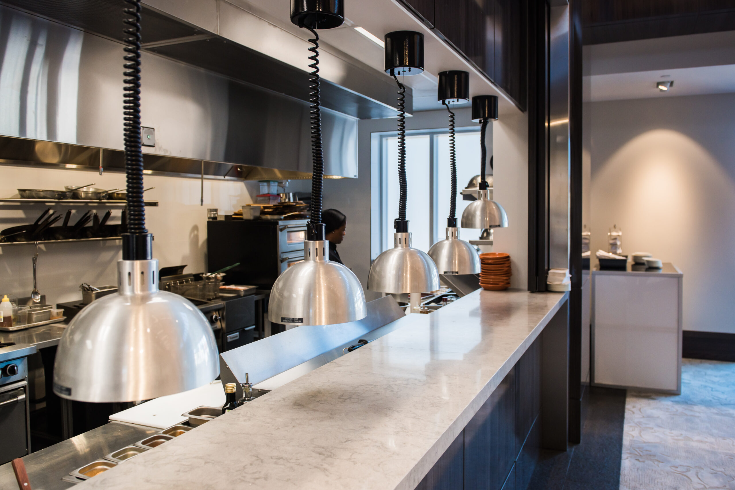 Commercial kitchen pass with heat lamps, stainless steel surfaces, and food preparation equipment.