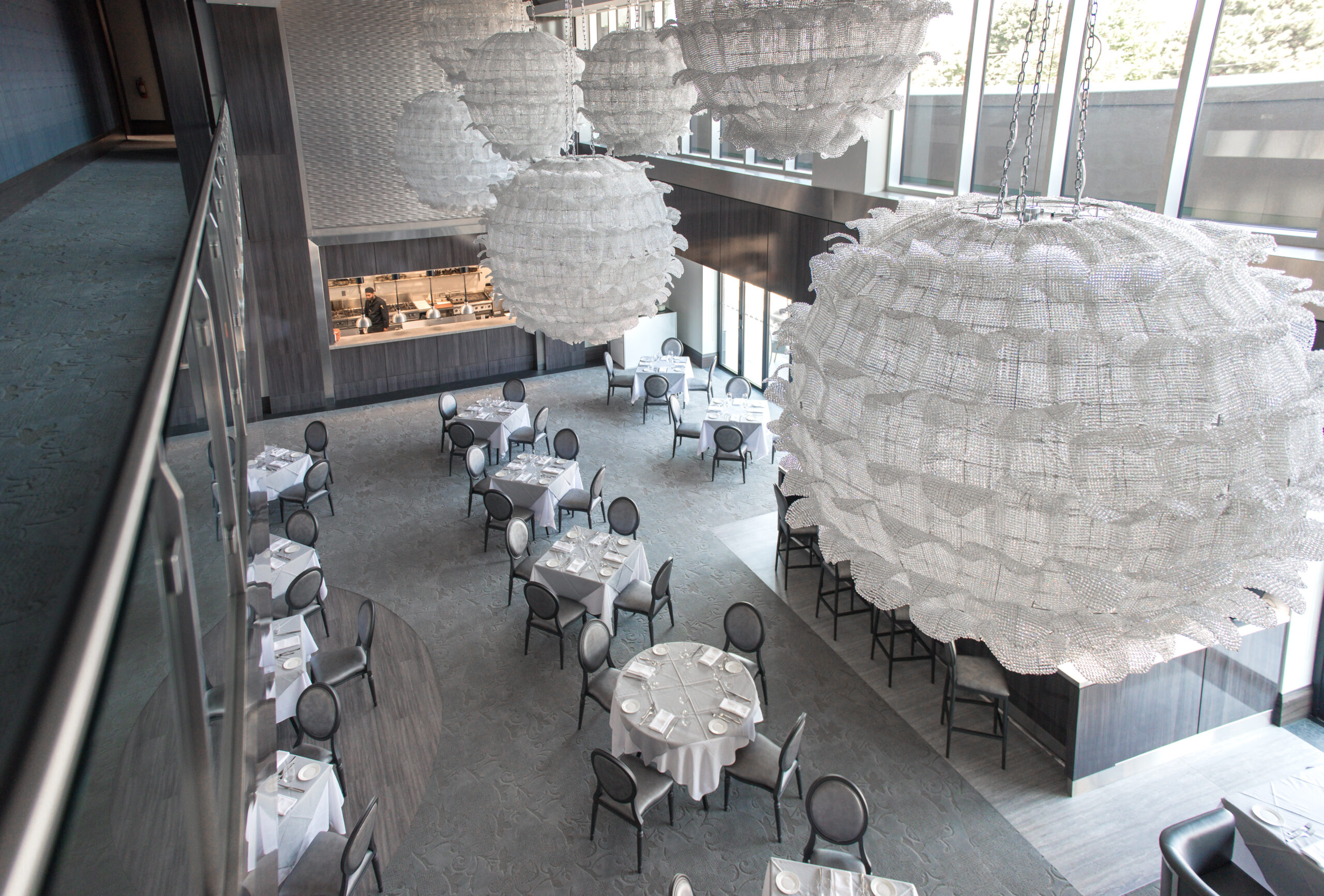 Interior event space with round dining tables, large decorative chandeliers, and tall windows.