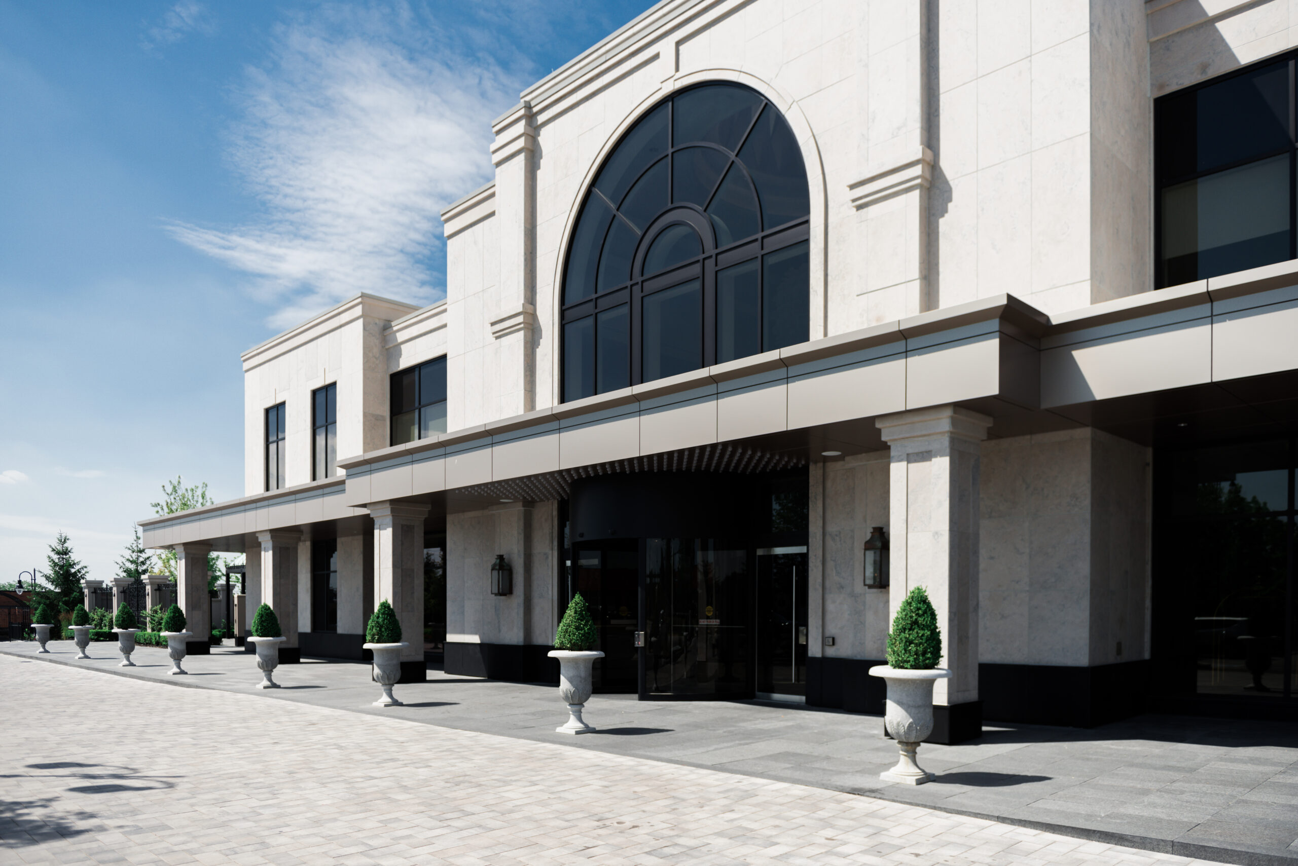 Exterior view of a formal event venue with a covered colonnade, arched windows, and decorative planters.