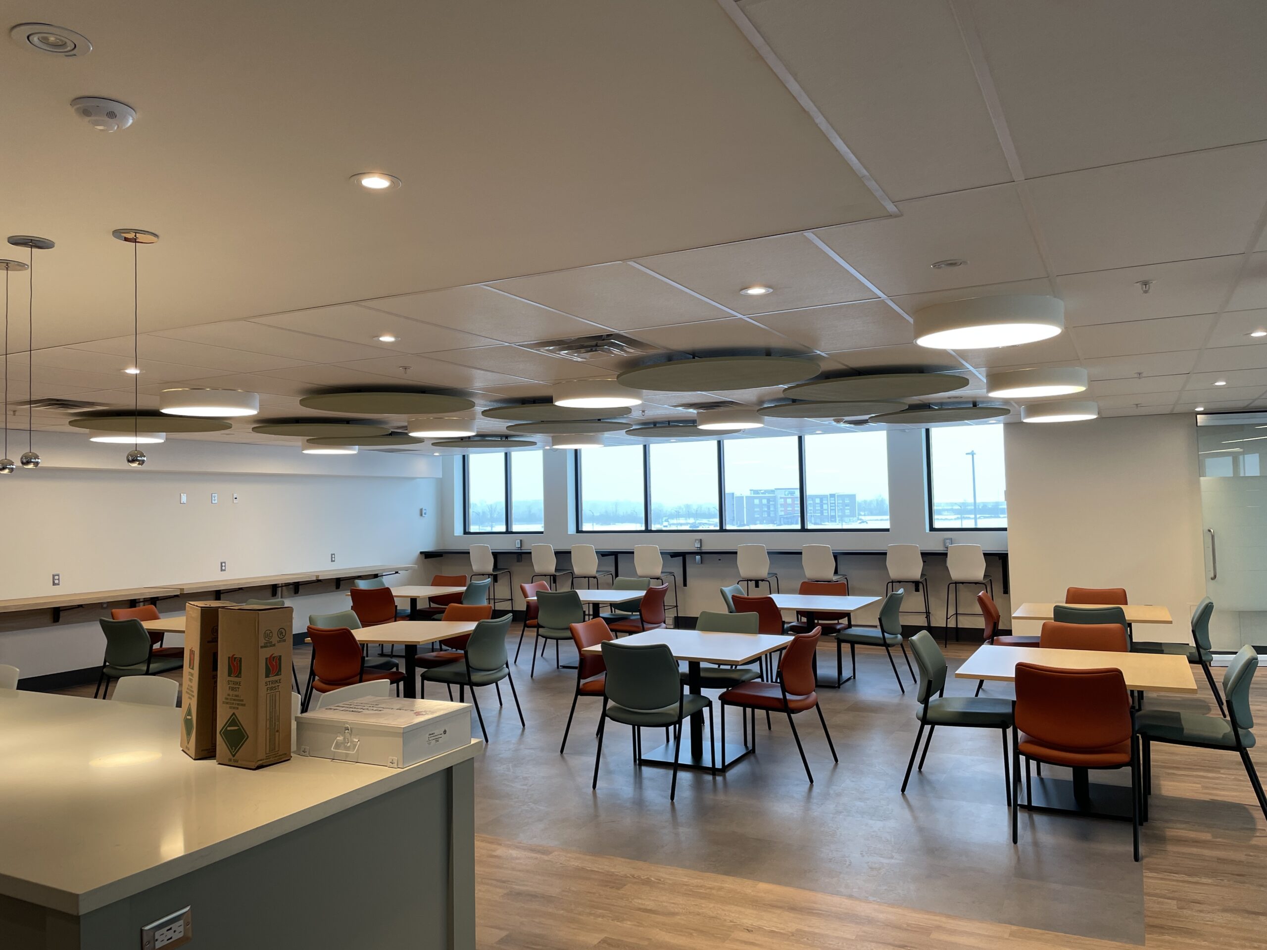 Interior seating area inside a Canadian Tire store with tables, chairs, pendant lighting, and large windows.