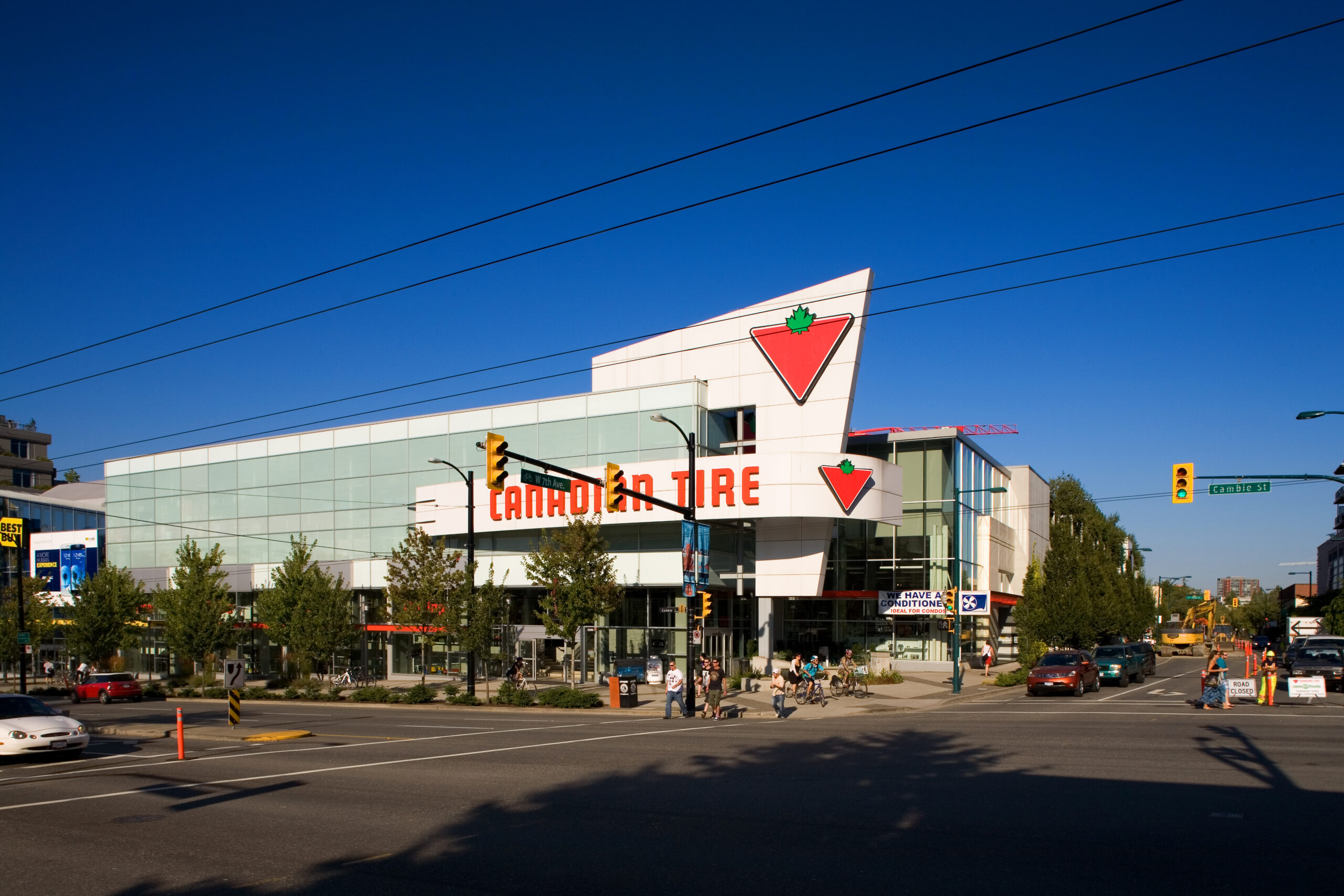 Street-level view of a Canadian Tire store with glass façade, branded signage, and surrounding city traffic.