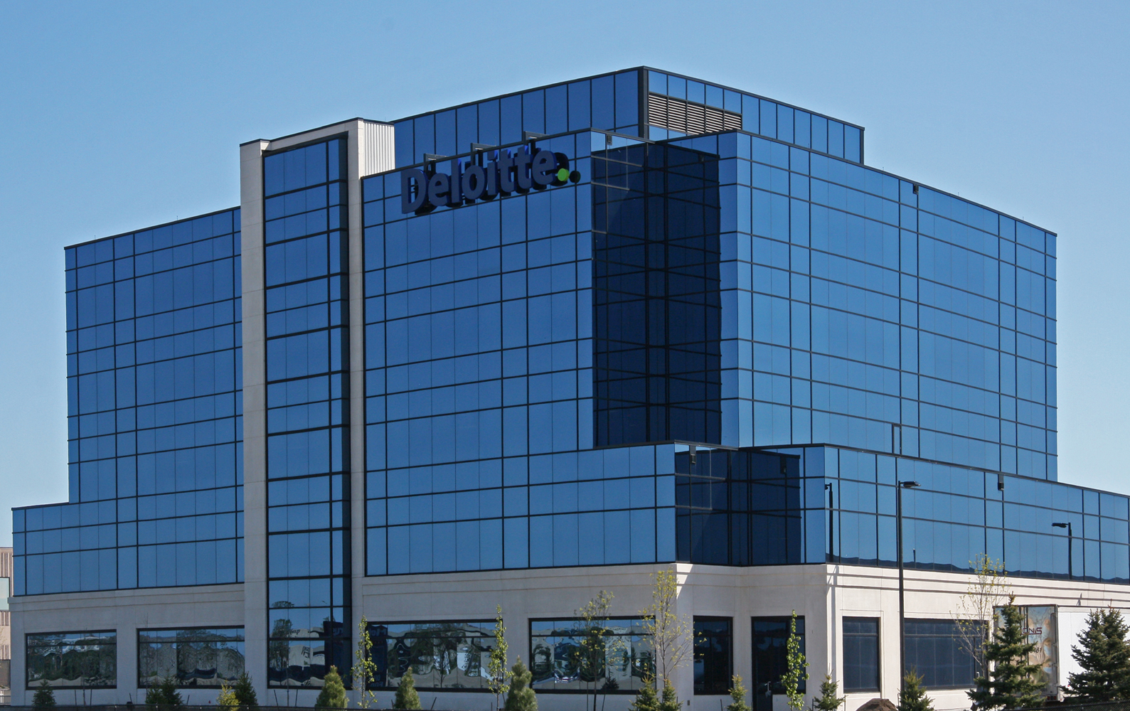 Exterior view of a multi-storey Deloitte office building with reflective glass windows and landscaped surroundings.