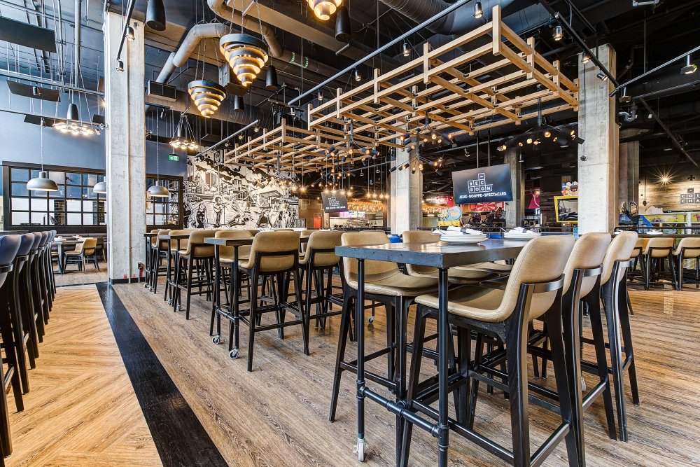 Modern bar and dining area with high-top tables, bar seating, and overhead lighting.